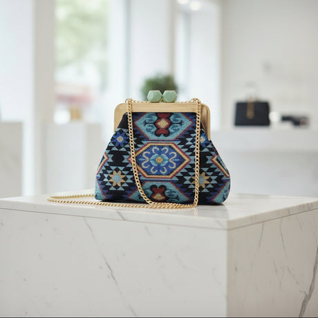 Blue embroidered frame bag on a marble block with its long gold chain