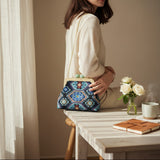 Seated woman in cream holding the navy patterned bag at her hip