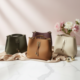 Four bucket handbags in olive, plum, tan and cream lined up against a pink backdrop with roses