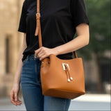 Tan bucket handbag carried crossbody with a black tee and blue jeans