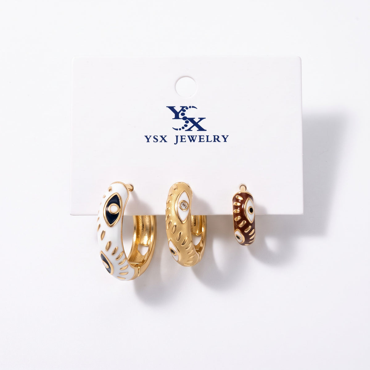 Three evil eye enamel hoop earrings in white, gold and brown in graduated sizes