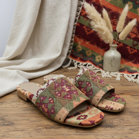 Pair of patterned handmade slippers on a glass shelf with a woven mat in the background
