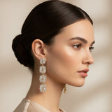 Pair of diamond-studded floral earrings worn by a woman on a beige background
