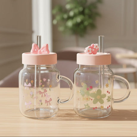 Two floral glass mugs with glass handles, pink lids and moulded bow and daisy toppers
