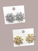 Two pairs of silver and gold flower-shaped earrings on display cards against a beige background