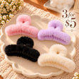 Four fluffy faux fur claw clips in pink, lilac, black and cream on a scalloped cream dish