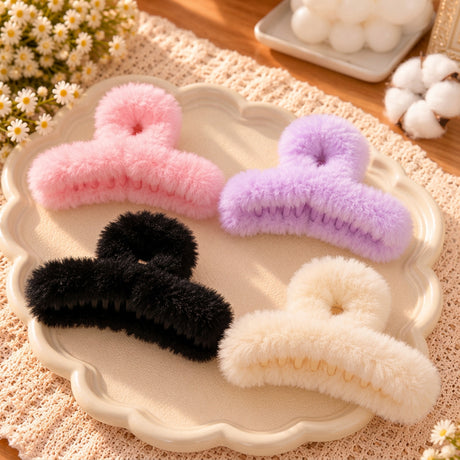 Four fluffy faux fur claw clips in pink, lilac, black and cream on a scalloped cream dish