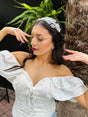 Woman in a white off-shoulder top with a decorative tiara, standing against a natural background