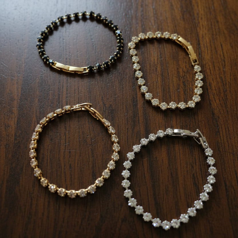 Four crystal square tennis bracelets on a wooden surface