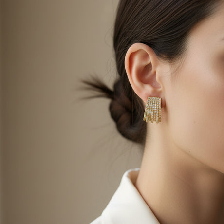 Gold fringe earrings worn by a woman on a beige background