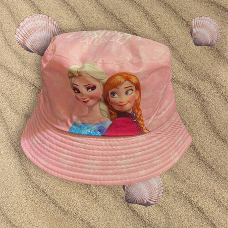 Pale pink bucket hat with Elsa and Anna artwork lying on rippled sand with seashells
