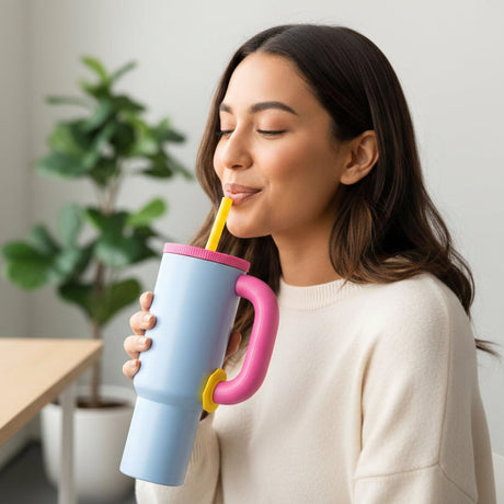 Pastel blue tumbler with a hot pink lid and handle and a yellow straw held in hand