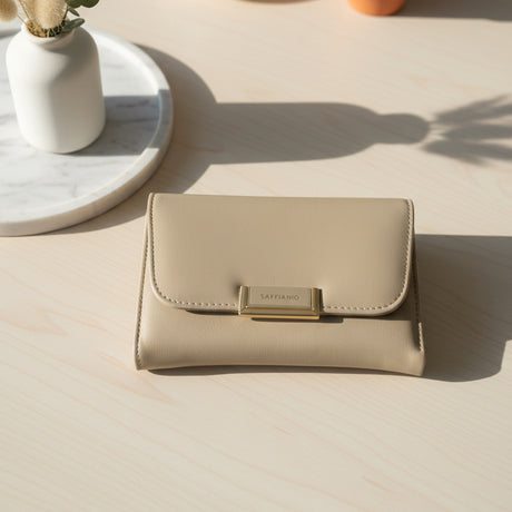 Beige wallet with gold clasp on a light wooden surface, with a plant vase in the background