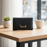 Black handbag on a wooden table with a cup of coffee and a plant in the background