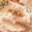 Three fuzzy claw clips in tan and cream with googly eyed creatures, knit hats and pom pom antennae