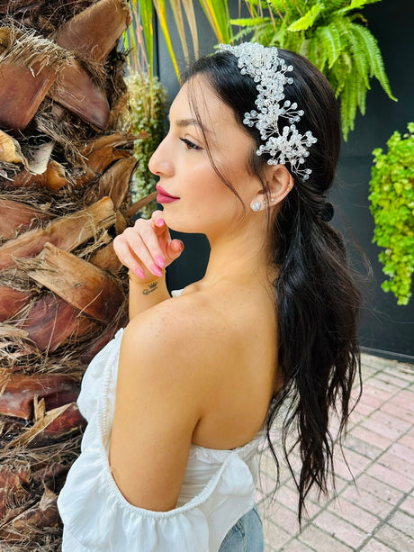 Woman with garden glow tiara and white top standing outdoors with plants in the background