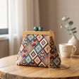 Geometric diamond weave handbag in red, navy and cream, green clasp, beside a coffee cup