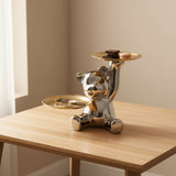 Chrome bear by a window with chocolate squares and a pink macaron in its raised gold tray