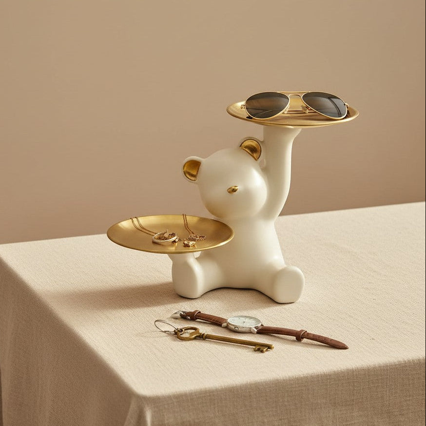 Cream bear with gold ears balancing sunglasses in its upper tray on a linen covered table