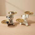 Two bear-shaped jewelry stands, one silver and one white, holding keys and rings on a wooden surface.