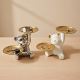 Two bear-shaped jewelry stands, one silver and one white, holding keys and rings on a wooden surface.