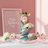 Bespectacled lady statue with a grey cone of carnations beside a pink picture frame