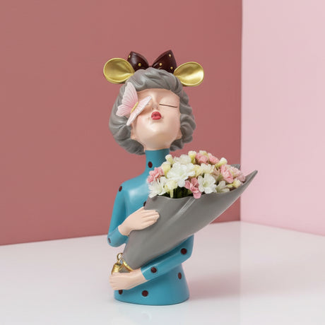 Teal polka dot dress, gold mouse ears and a butterfly on her nose above a grey cone vase