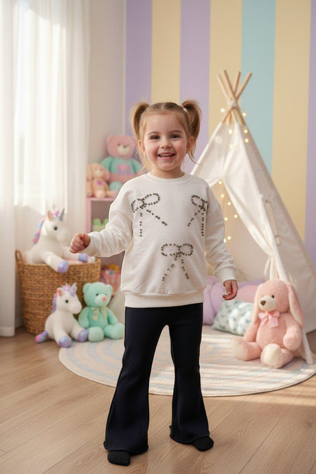 Girl in a cream rhinestone bow sweatshirt and navy flared pants