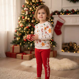 Young girl holding a small gift in a white festive print top and red leggings by a Christmas tree