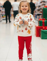 Smiling girl in a white holiday print top and red leggings standing in a store aisle beside gift boxes