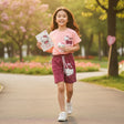 Young girl in a park wearing a Hello Kitty outfit, holding a book and plush toy.