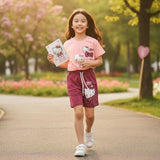 Young girl in a park wearing a Hello Kitty outfit, holding a book and plush toy.