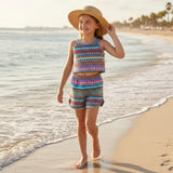 Young girl in a colorful outfit and straw hat standing on a beach.