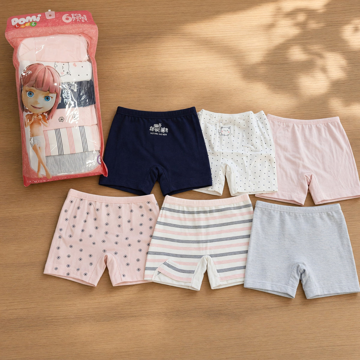 Six girls boxer shorts in navy, pink, grey, polka dots and pink stripes laid out beside their pack