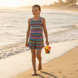 Young girl in a colorful swimsuit walking on a beach with a bucket.