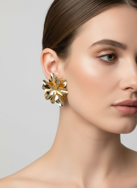 Woman wearing a gold floral design earring against a plain background