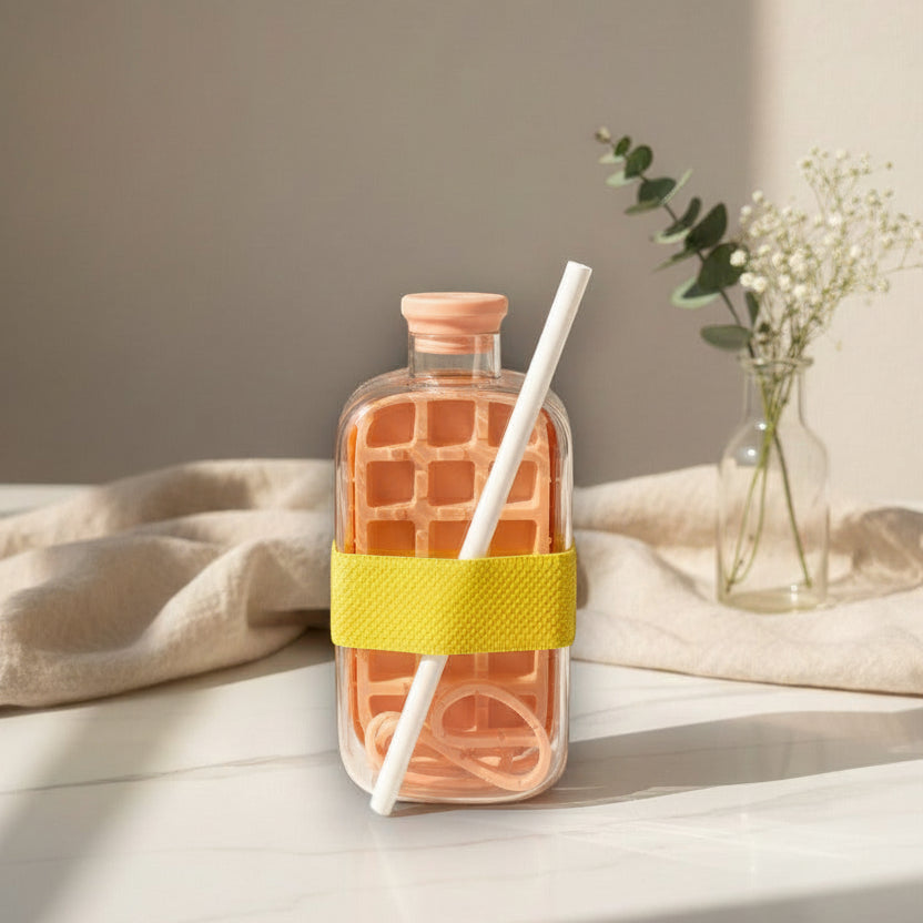 Coral glass drink bottle with a yellow silicone band and a white straw