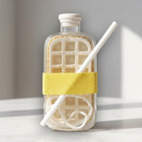 Clear glass drink bottle with a yellow silicone sleeve, white straw and cream chiller insert