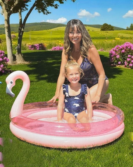 Pink two ring paddling pool with glitter confetti vinyl and a flamingo head backrest, child sitting in water