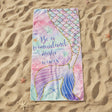 Pastel pink and mint beach towel with a gold outlined mermaid tail on sand