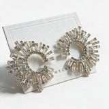 Pair of gold baguette crystal sunburst earrings with a pave inner ring on a white card