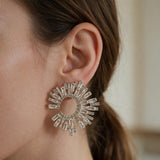 Gold sunburst open circle earring with radiating baguette crystals worn on the ear