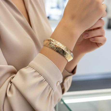 Gold bangle bracelet on a person's wrist with blurred background