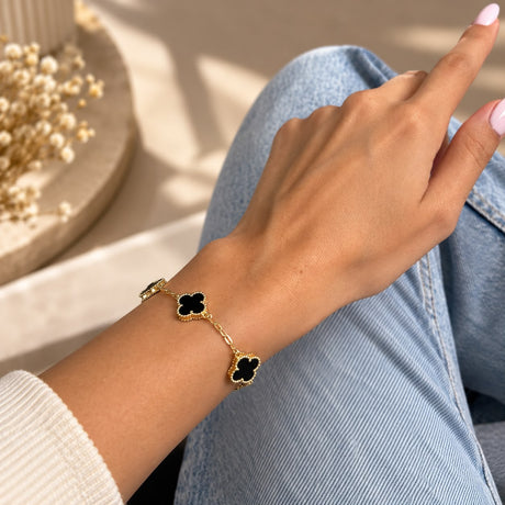 Close up of a black clover station bracelet with beaded gold edges worn over jeans