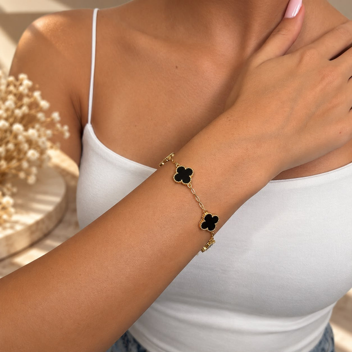 Gold tone bracelet with black clover charms on the wrist, hand resting on the shoulder