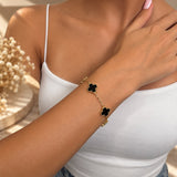 Gold tone bracelet with black clover charms on the wrist, hand resting on the shoulder