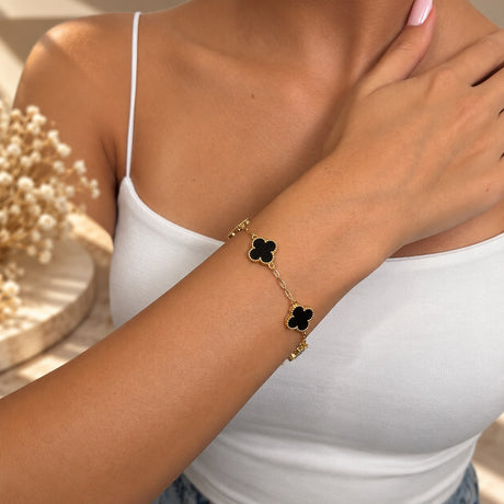 Gold tone bracelet with black clover charms on the wrist, hand resting on the shoulder