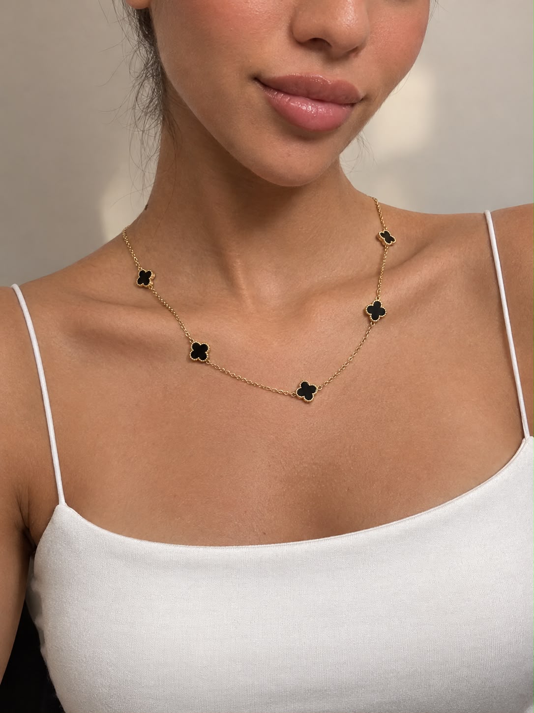 Close up of black clover charms with beaded gold edges along a fine chain