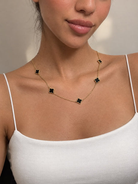 Close up of black clover charms with beaded gold edges along a fine chain
