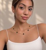 Dainty gold chain necklace with black clover charms against a sunlit wall
